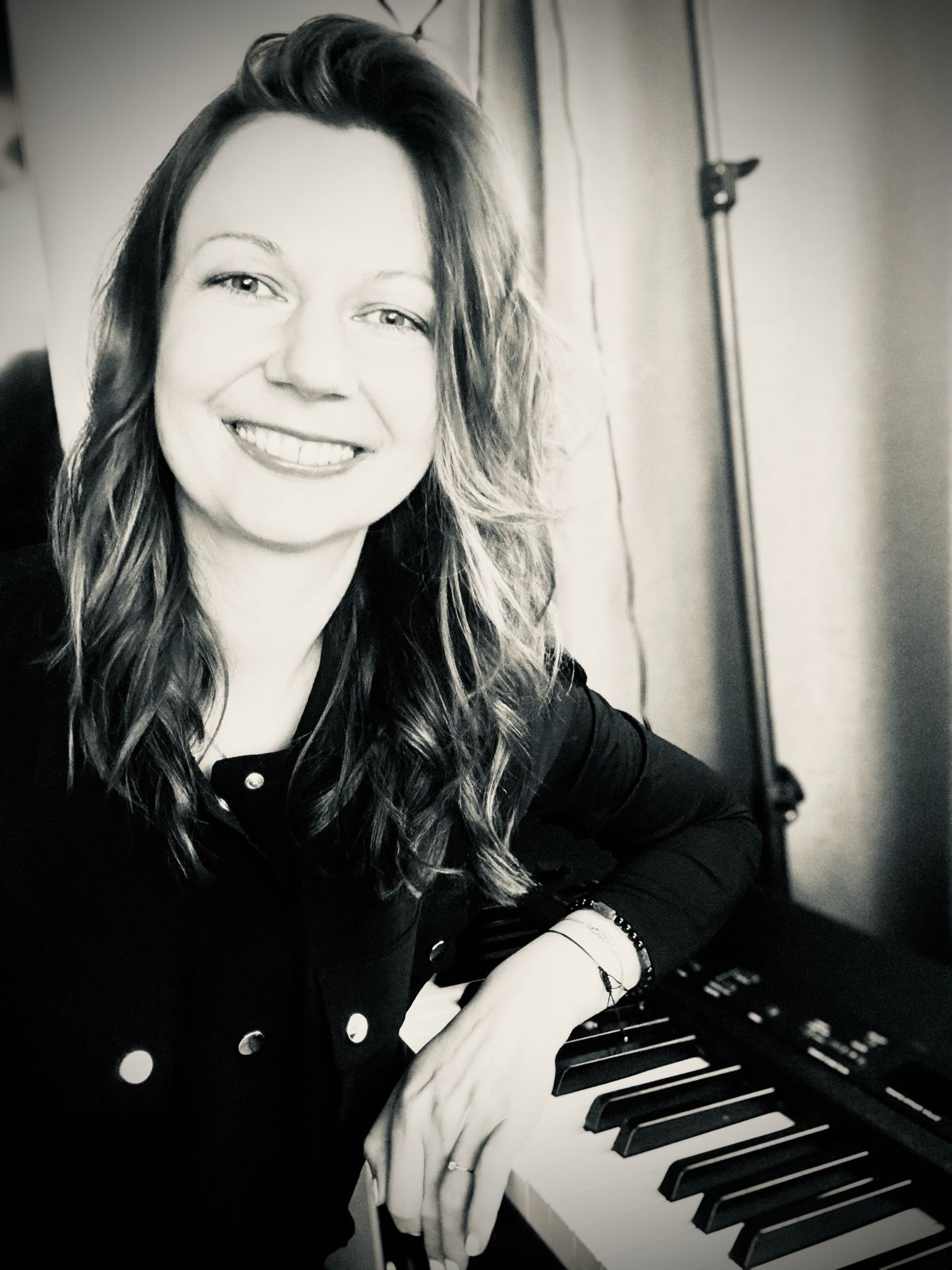 Agi, founder of Agi and the Keys, smiling beside a piano